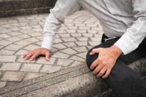 A person is on their hands and knees, wondering who is responsible for a sidewalk trip and fall injury