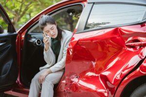 A woman on the phone in a damaged car. Learn about whether you should call the police after a car accident in New York.