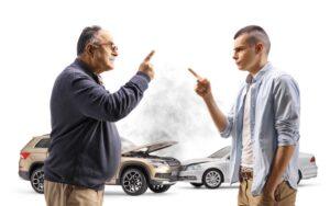 Two drivers argue beside their cars after a crash, with both wondering what will happen since each was partially at fault for the car accident.