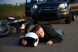 A motorcycle rider lies on the pavement after a crash and wonders who is at fault for most motorcycle accidents.