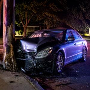 Sedan with a crumpled front end against a utility pole at night with police lights