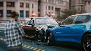 Two cars that have just collided with each other head-on. The drivers are standing outside their cars; one on the phone, the other taking a photo of the motor vehicle collision damage.